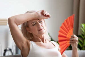 Older women overheated waving an orange fan to cool of from hot flash