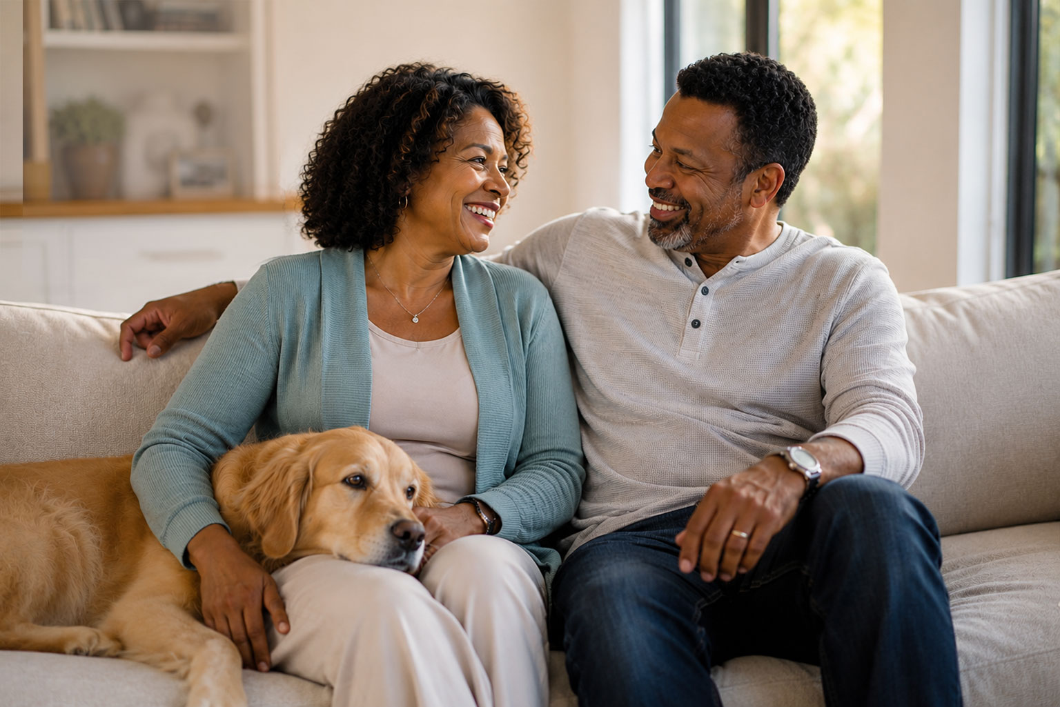 Middle-aged Black couple relaxing together on a sofa with their golden retriever, reflecting comfort, connection, and improved well-being during menopausal hormone therapy.